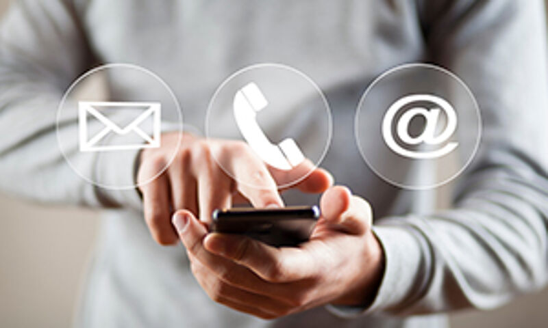 "Eine Männerhand hält ein Smartphone, auf dessen Display Symbole für Telefon, E-Mail und Chat zu sehen sind – symbolisch für die Kontaktaufnahme."