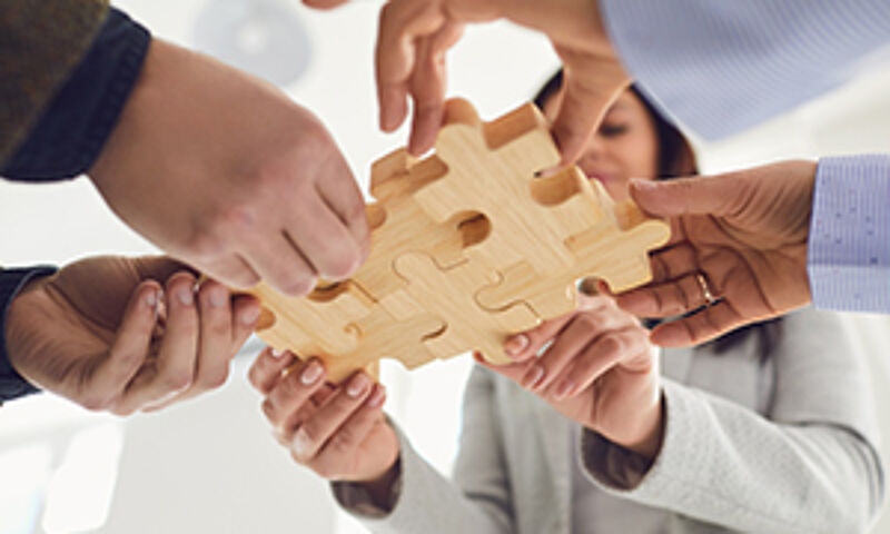 "Mehrere Menschen halten gemeinsam Puzzleteile in die Mitte des Bildes – symbolisch für Zusammenarbeit und berufliche Entwicklung."