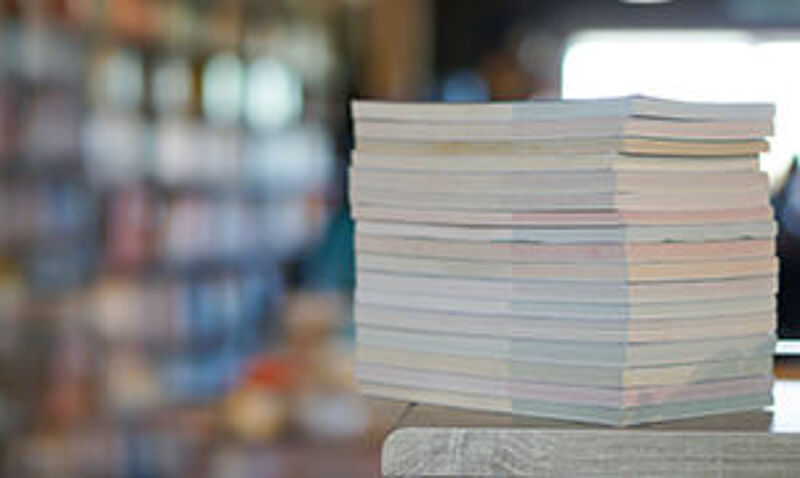 "Symbolbild für Veröffentlichungen – ein hoher Stapel Papierunterlagen liegt auf einem Tisch, im Hintergrund unscharf ein heller Raum."