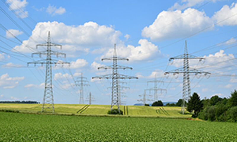 "Strommasten in einer weiten Landschaft mit Raps und grünen Feldern – Symbolbild für zuverlässige Energieversorgung und Infrastruktur."
