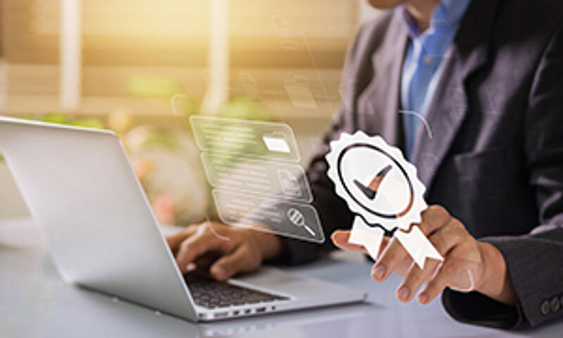 "Ein Mann arbeitet am Laptop, neben dem Laptop ist ein Icon für Qualitätssicherung und Zertifizierung eingeblendet – symbolisch für ISO-Standards und Qualitätskontrolle."